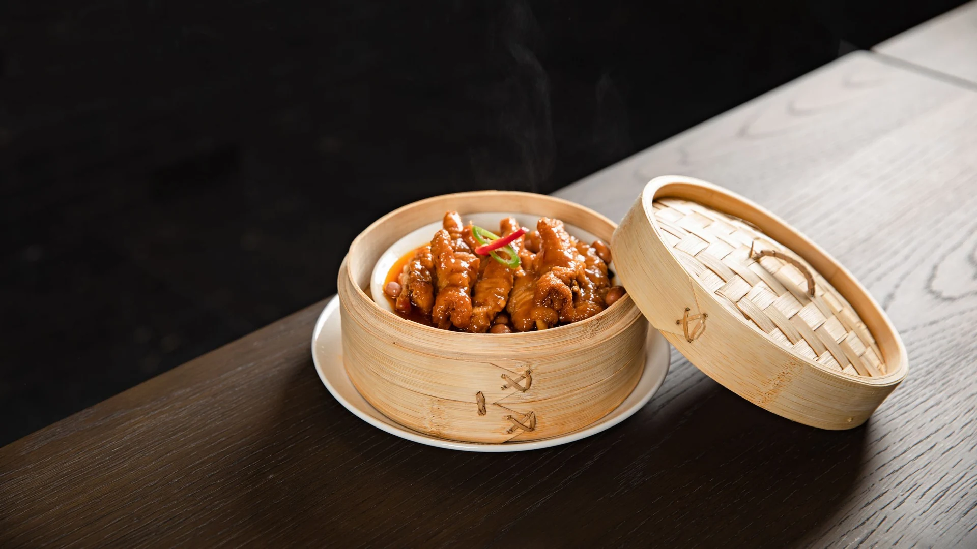 A steaming savoury dish in a bamboo basket on a wooden table.