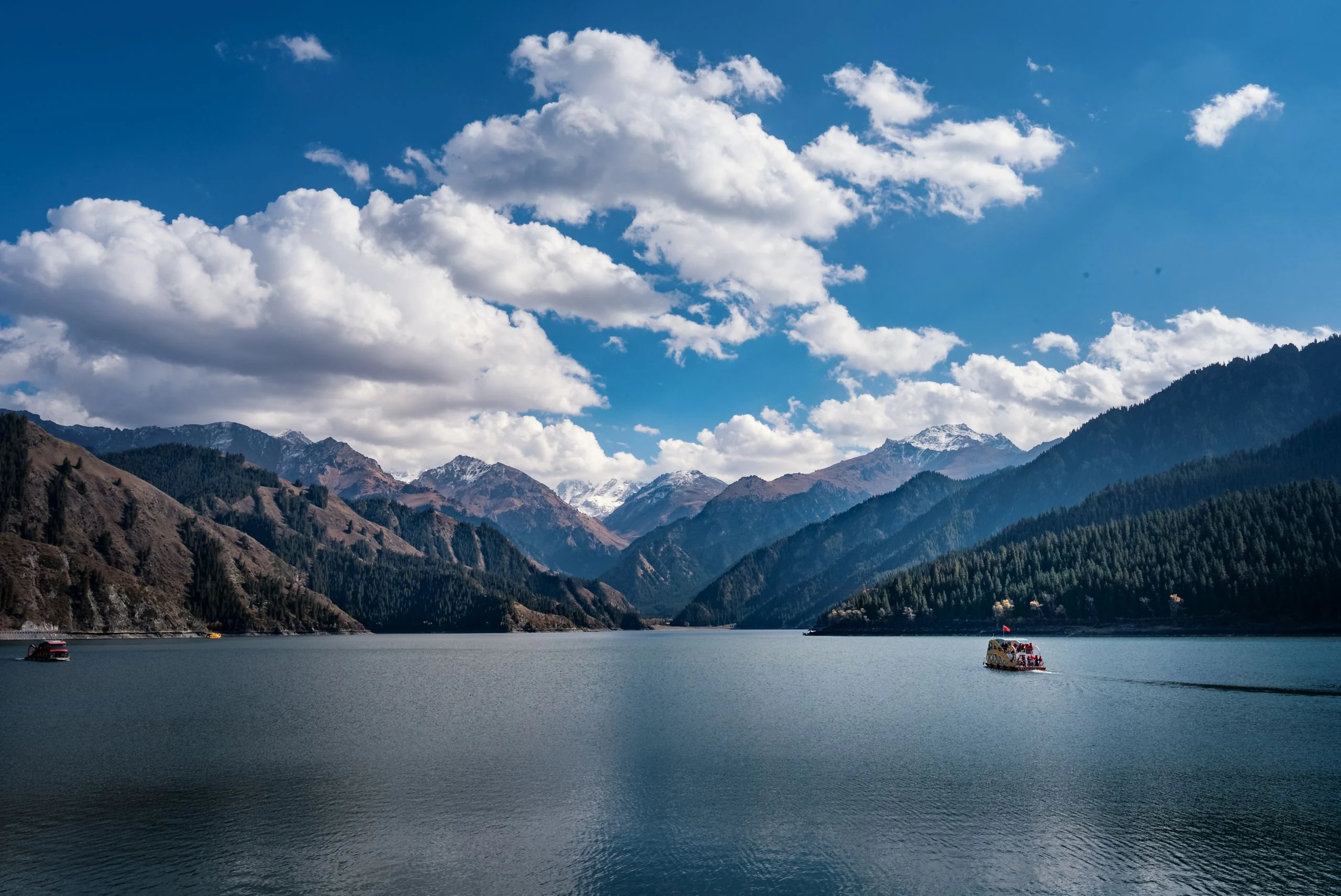 Snow-dusted Tianshan peaks, open sky and boats on Tianchi Lake.