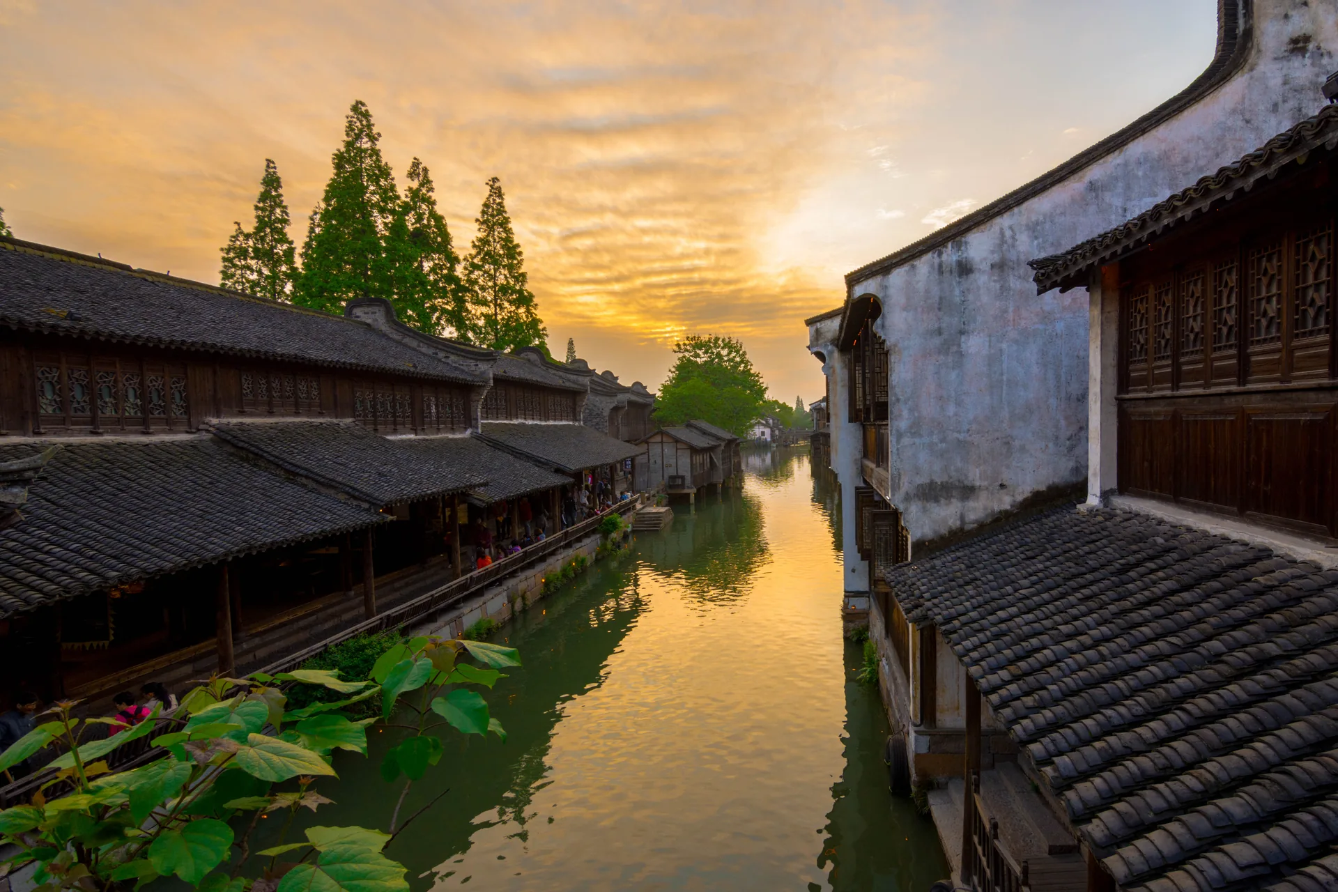 A canal in Zhouzhuang, Jiangsu, with pale walls, layered tiled roofs and warm sky reflected between the two banks.